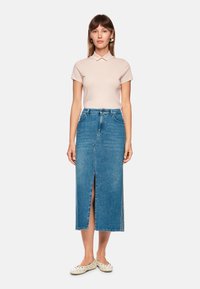 Denim skirt with a front slit, light blue color, straight shape, and waistband. Paired with a short-sleeve pale pink top and flat shoes.