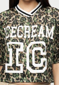 Κοντομάνικη φόρμα πλέγματος καμουφλάζ με μαύρο, πράσινο και καφέ μοτίβο, λευκό ριγωτό V-λαιμόκοψη και μεγάλο λευκό αριθμό "16" και κείμενο "ICECREAM" στο εμπρόσθιο μέρος.