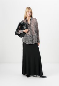 Blusa de tecido leve com padrão de leopardo e fecho com botões, combinada com uma saia preta até ao chão. O modelo segura uma bolsa preta e volumosa, usando sapatos de salto pretos.