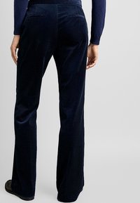 Granatowe spodnie z sztruksu w kształcie dzwonów z ząbkowanym wzorem, posiadające dwie tylne kieszenie. Materiał ma subtelny połysk i dopasowany krój.