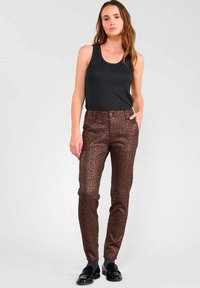 Pantalons slim en imprimé léopard marron avec un bouton marron et des poches avant, associés à un haut sans manches noir. Texture brillante et coupe apurée.