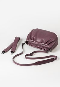 Lila Lederhandtasche mit einem gerafften Design, ausgestattet mit einem Reißverschluss oben, abnehmbaren Trägern und einer glatten Textur. Zwei verstellbare Träger sind enthalten.