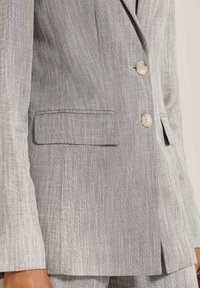 Grauer Leinen-Blazer mit strukturiertem Design, zwei Knöpfen und einer einzelnen Tasche auf der linken Seite. Texturiertem Stoff mit einem subtilen Glanz.