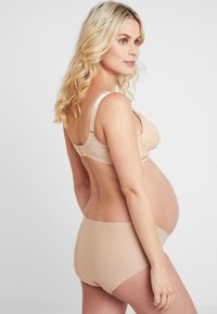 Nude graviditets-BH med blonderdetaljer, justerbare stropper og en jevn bakside. Kombinert med matchende nude sømløse truser.