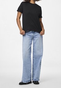 Svart bomullströja med korta ärmar, kombinerad med ljusblå vida jeans med en blekt tvätt. Svarta skor med tjock sula fulländar looken.