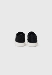 Încălțăminte sport din suede negru, cu o talpă din cauciuc alb, având un design cu vârf jos și cusături contrastante pe toc și lateral.