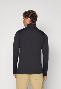 Black long-sleeve athletic top with a textured pattern, high collar, and fitted design. Features contrasting sleeve cuffs and shoulder panels.