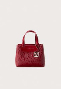 Sac à main en cuir verni rouge avec motif logo en relief, forme structurée, double poignées, et un tag d'accent argenté suspendu.