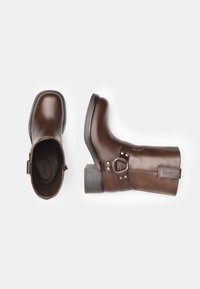 Bruine leren enkellaarzen met een vierkante neus, stevige hak, decoratieve riem met gespdetail en een gladde textuur.