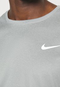 Camiseta Nike gris con cuello redondo, tejido texturizado y logo blanco en el área del pecho izquierdo.