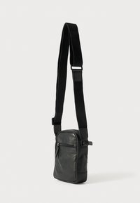 Mala de tiracolo em couro preto com alça ajustável, bolso frontal com fecho de correr, formato retangular, textura lisa e design minimalista.