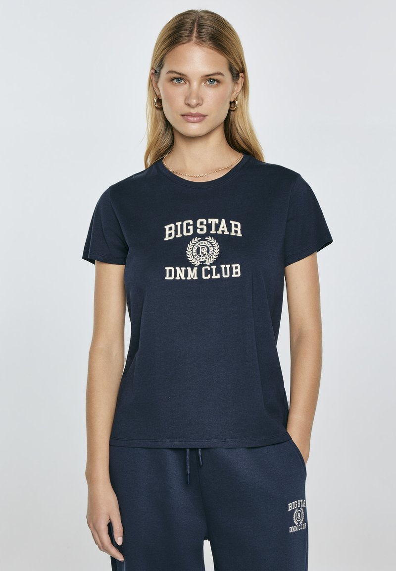 Tamsiai mėlynas medvilnės T-shirts su trumpomis rankovėmis ir apvaliu kaklu. Viduryje esančioje baltos spalvos grafikoje užrašyta "BIG STAR DNM CLUB" su akcentais.