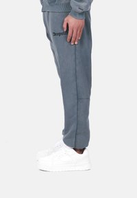 Joggers en coton gris avec poches latérales et un détail de couture surélevé, associés à des baskets blanches. Logo "Dropsize" brodé sur la cuisse.