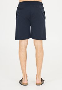 Mörkblå shorts med elastisk midja, två bakfickor och en strukturerad tygfinish. Bärs med mörka sandaler med öppen tå.
