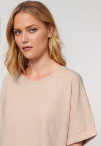 Una giovane donna con lunghi capelli biondi e mossi indossa un top leggero e strutturato, guardando direttamente l'osservatore con un'espressione sottile.