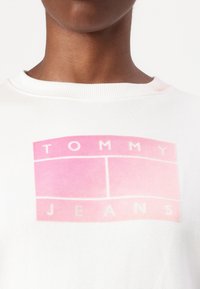 Witte sweatshirt met een roze-gradient ontwerp van het logo in een doosvorm, met "TOMMY" bovenaan en "JEANS" eronder in witte tekst. Gemaakt van katoen, met een ronde hals.