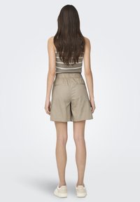 Shorts beige al ginocchio con vita elastica, abbinati a una maglietta a righe. Le scarpe sono di colore chiaro, con una texture liscia.