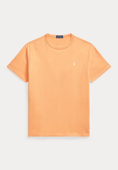 Απλό πορτοκαλί κοντομάνικο T-shirt με στρογγυλή λαιμόκοψη, με μικρό λευκό κεντημένο λογότυπο στο αριστερό μέρος του στήθους και μια μπλε ετικέτα μέσα στο γιακά.