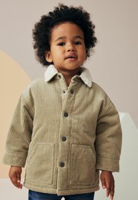 Giacca in corduroy beige con colletto in sherpa bianco, bottoni a pressione e due tasche frontali. Presenta una texture a coste e una vestibilità comoda.