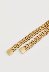 Δύο χρυσές αλυσίδες με επίπεδους τετράγωνους κλιπ σε φωτεινή επιφάνεια, μία αλυσίδα με μεγάλους συνδέσμους και η άλλη με μικρές στρογγυλές χάντρες.