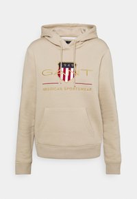 Felpa beige con tasca frontale, cordoncini e logo scudetto GANT ricamato con la scritta "1949" e "American Sportswear" sul petto.