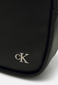 Czarna skórzana torba o fakturowanej powierzchni. Posiada metaliczne srebrne logo "cK" w dolnym rogu oraz wyraźny kształt.