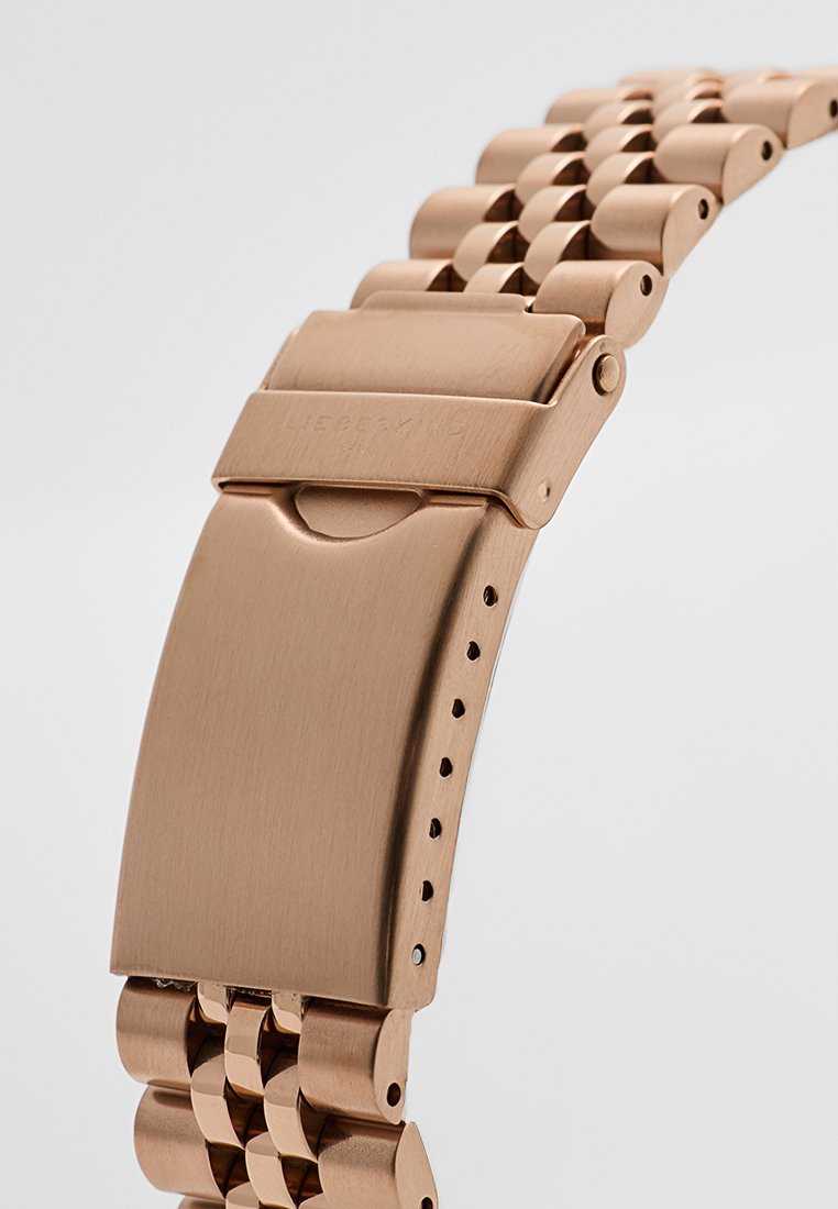 Pulsera de reloj de metal bronceado con eslabones de acabado suave y cierre desplegable. El diseño incluye agujeros de ajuste distribuidos de manera uniforme.