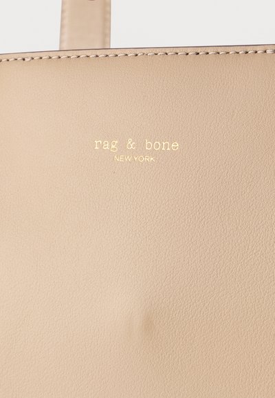 Μπεζ δερμάτινη τσάντα με ραμμένη άκρη και ανάγλυφο χρυσό λογότυπο "rag & bone NEW YORK" κοντά στο πάνω κέντρο.