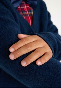 Marineblauer Strickcardigan mit weichem Textur, der einen sichtbaren Hand zeigt, die auf dem Ärmel ruht. Darunter ist ein kariertes Hemd teilweise sichtbar.