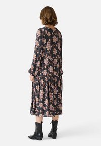 Long-sleeve black dress with pink floral pattern, tiered design, and ruffled cuffs, paired with black ankle boots.