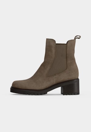 Bottine Chelsea en daim marron avec panneaux latéraux élastiques, une languette à l’arrière, et un talon et une semelle noirs et épais.
