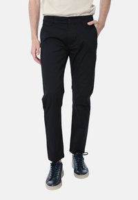 Chinos neri in cotone con vestibilità slim, dotati di chiusura con bottone e tasche laterali. Abbinati a sneakers blu navy.