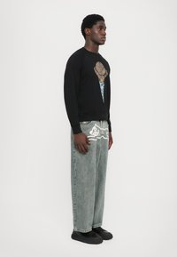 Zwarte sweatshirt met een graphic van een ijscoman, gecombineerd met lichtblauwe denim wijde jeans met witte visgraatrand en zakken.