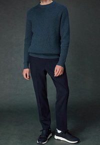 Granatowy sweter z prążkowanej dzianiny w połączeniu z dopasowanymi ciemnymi spodniami i sportowymi czarnymi sneakersami z białymi akcentami. Gładkie tekstury i dopasowany krój.