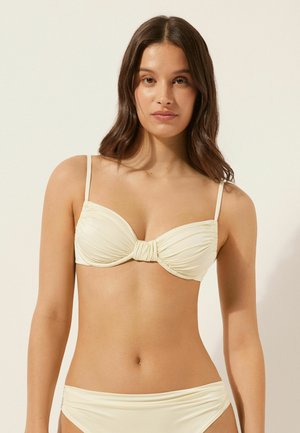 Krämgul bikiniöverdel med rynkad tyg, underwire-stöd och tvinnad framdetalj. Justerbara band och matchande botten.