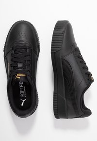 Chaussures en cuir noir avec une finition texturée, bout rond et semelle en caoutchouc surélevée. Présente des lacets plats noirs et un logo doré sur la languette.