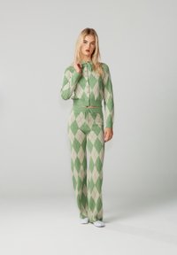 Zöld és bézs átlós mintájú kötött kardigán gombokkal, hozzáillő, elasztikus derékpántos nadrággal párosítva.