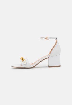 Sandale blanche à talon avec bride à la cheville, talon bloc, bout ouvert et détail décoratif en chaîne dorée sur la bride avant.