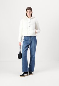 White puffer jacket with a hood, featuring a quilted design and front buttons. Paired with blue wide-leg jeans and black sneakers.