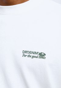 Witte katoenen t-shirt met een groen logo en de tekst "DRDENIM® For the good times" en een bloemontwerpelement.