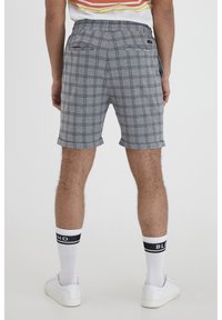 Shorts à carreaux gris et noirs avec une taille élastique et deux poches arrière, associés à des baskets blanches et des chaussettes avec une rayure noire.