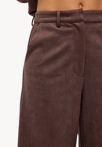 Pantalon en tissu marron doux avec une texture lisse, doté d'une ceinture ajustée, de poches latérales et d'une coupe sur mesure.