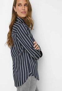 Camicia a righe blu navy con righe verticali bianche, maniche lunghe e colletto a punta. Presenta una vestibilità comoda e spacchi laterali all'orlo.