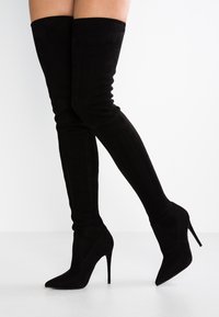 Stivali neri in suede, al ginocchio, con punta affilata e tacco a stiletto. Texture liscia, gambo aderente e costruzione senza cuciture.