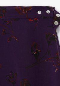 Tessuto viola con motivi floreali in rosso e oro, dotato di bottoni a pressione argentati e di una zip sul lato. Texture liscia.