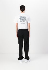 Witte t-shirt met een kleurrijk grafisch ontwerp op de achterkant. Gecombineerd met zwarte cargo-broeken en witte sneakers. Eenvoudige, casual outfit.