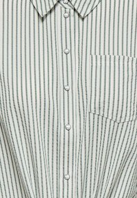 Chemise boutonnée avec des rayures verticales vertes et blanches, col et poche poitrine. Le tissu semble doux avec une texture lisse.