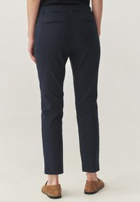 Morne slim-fit hlače iz gladkega blaga, z zadnjimi žepi in rahlo zoženimi nogami, v kombinaciji s rjavimi loafers.
