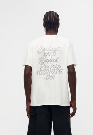 Uomo con capelli intrecciati indossa una t-shirt bianca con testo grigio "Carhartt WIP Rugged Precision (03010761-061)" sulla schiena e pantaloncini cargo neri.