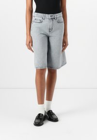 Ljust grå denimbermuda-short med knielängd, klassisk femficksdesign och subtil blekning. Bärs med svarta loafers och vita strumpor.